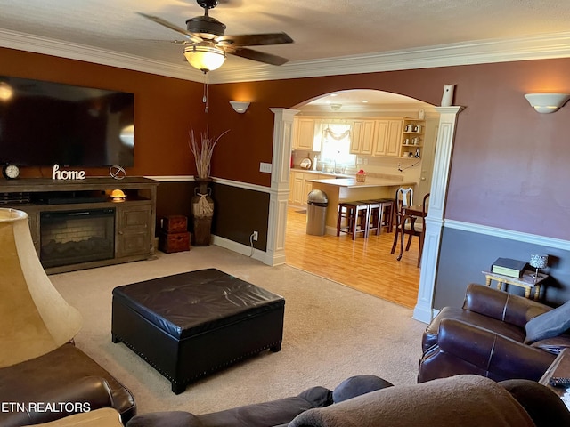 carpeted living room featuring sink, ornamental molding, ceiling fan, and ornate columns