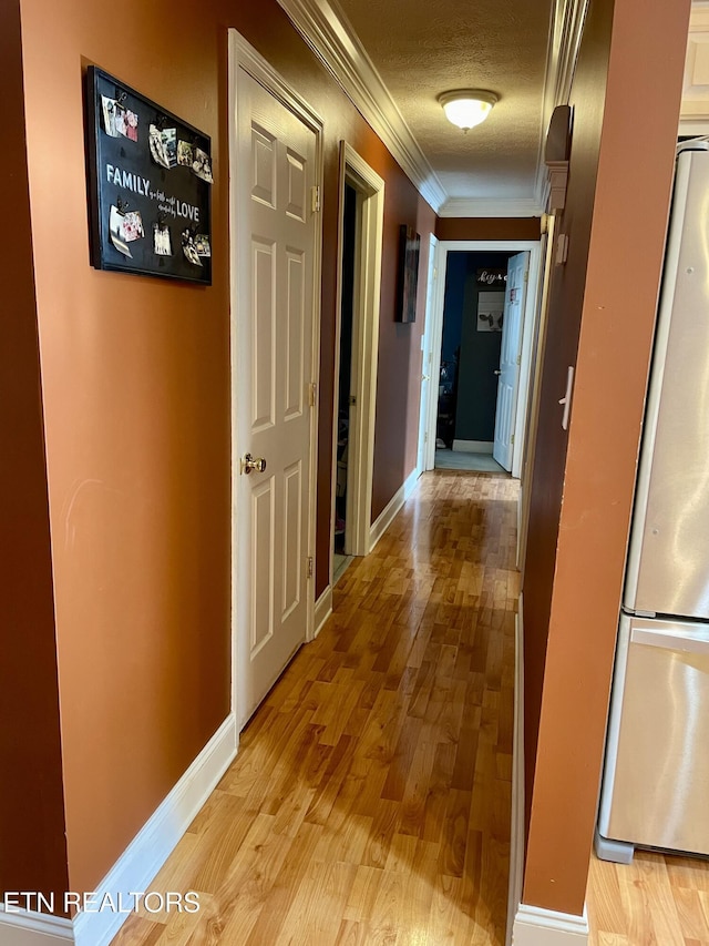 hallway featuring crown molding, light hardwood / wood-style floors, and a textured ceiling