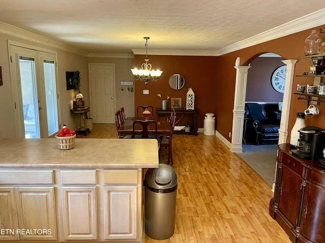 kitchen featuring decorative columns, a chandelier, hanging light fixtures, crown molding, and light wood-type flooring