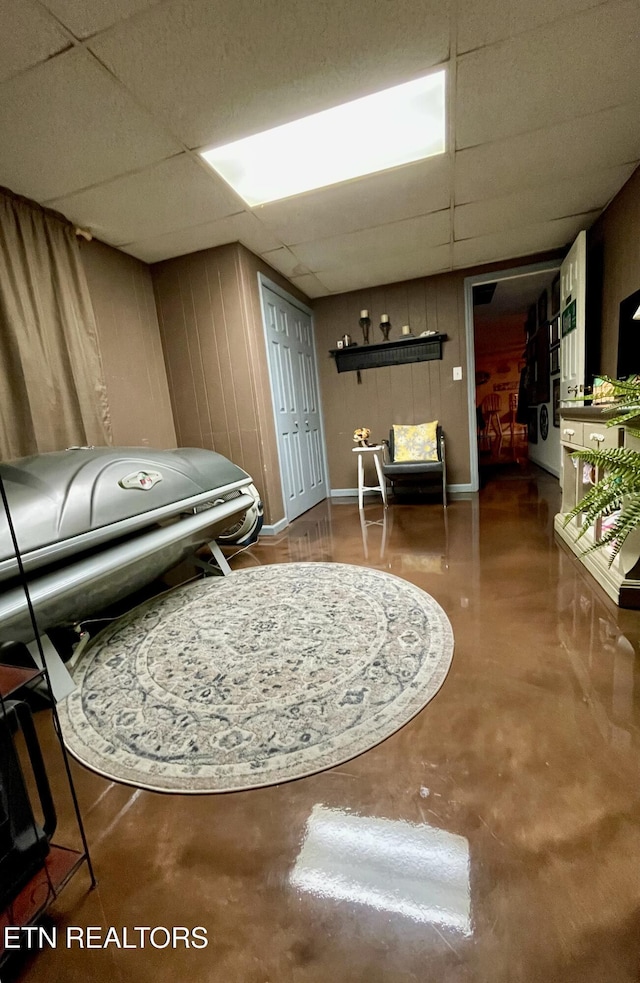 living area with a paneled ceiling, concrete floors, and wood walls