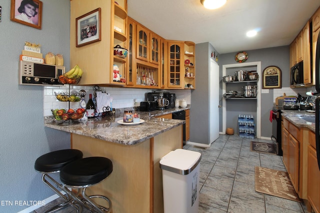 kitchen with a kitchen breakfast bar, tasteful backsplash, black appliances, kitchen peninsula, and dark stone counters