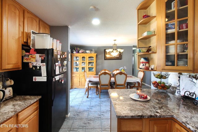 kitchen with an inviting chandelier, decorative light fixtures, black refrigerator, dark stone counters, and decorative backsplash