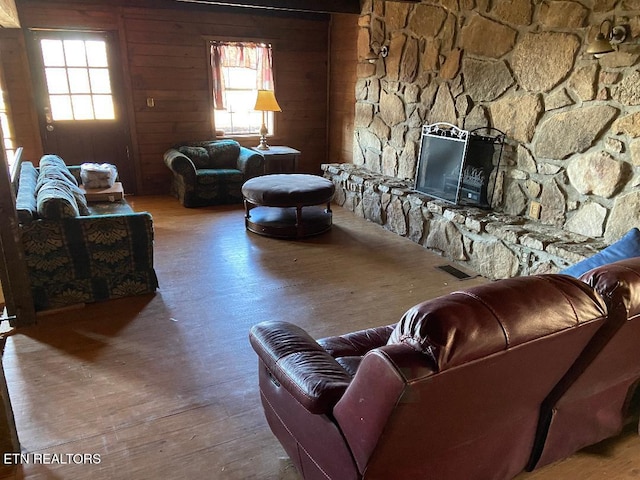 living room featuring a stone fireplace, wood-type flooring, wooden walls, and a healthy amount of sunlight