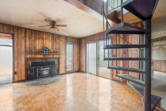 unfurnished living room with a textured ceiling, wooden walls, stairs, and ceiling fan