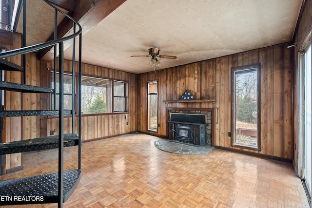 unfurnished living room featuring wood walls, a textured ceiling, baseboards, and a ceiling fan