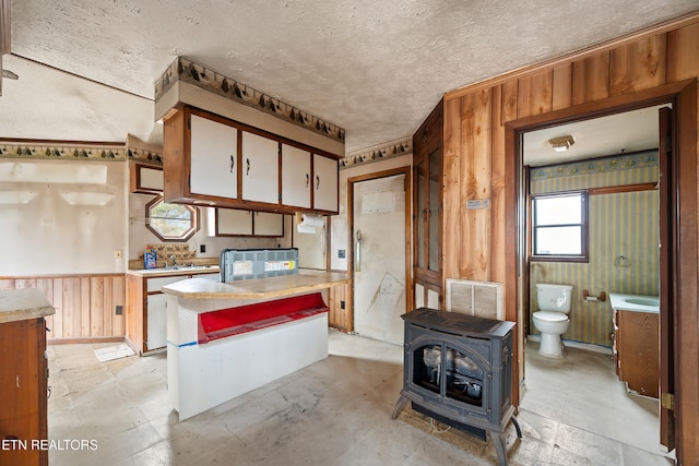 kitchen with visible vents, a textured ceiling, wood walls, light countertops, and a wood stove