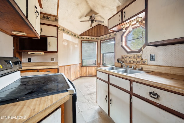 kitchen with a wainscoted wall, lofted ceiling, electric range, ceiling fan, and a sink