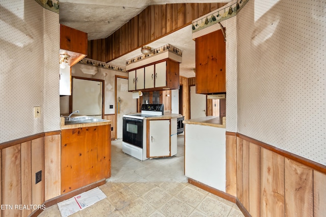 kitchen with light floors, a wainscoted wall, wallpapered walls, electric range, and a sink