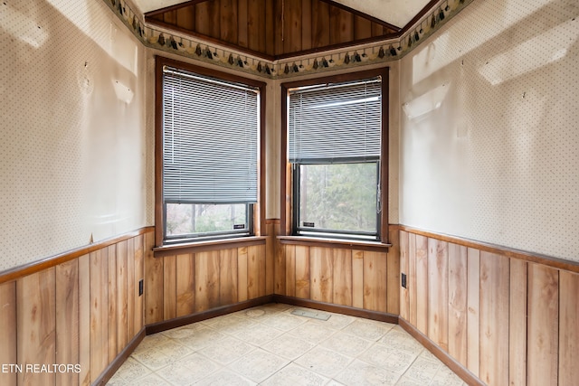 unfurnished room with wallpapered walls, lofted ceiling, and wainscoting