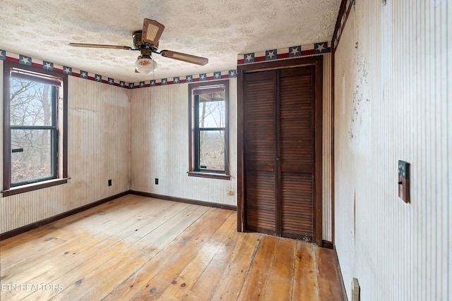 unfurnished bedroom featuring ceiling fan, light wood-style flooring, baseboards, and a textured ceiling