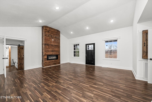 unfurnished living room featuring dark wood-type flooring, a large fireplace, lofted ceiling, and a barn door