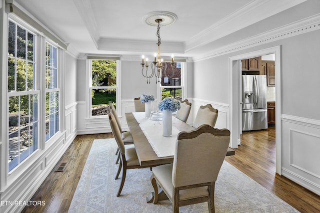 dining room featuring a wainscoted wall, a tray ceiling, wood finished floors, and visible vents