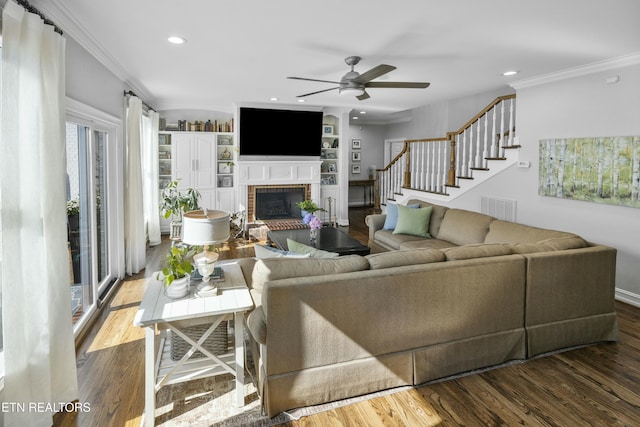 living room with visible vents, stairway, ornamental molding, wood finished floors, and a brick fireplace