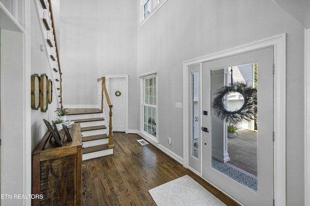 foyer featuring wood finished floors, visible vents, a towering ceiling, baseboards, and stairway