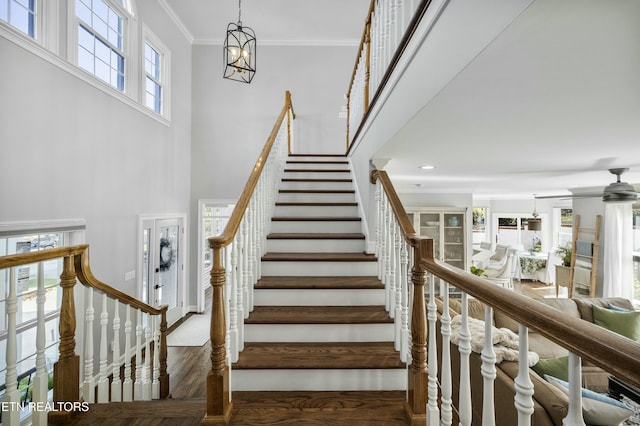 stairs with crown molding, a towering ceiling, and ceiling fan with notable chandelier