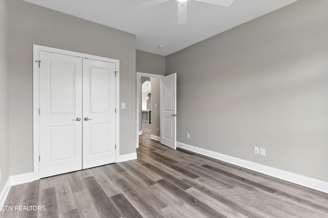 unfurnished bedroom with wood-type flooring, ceiling fan, and a closet