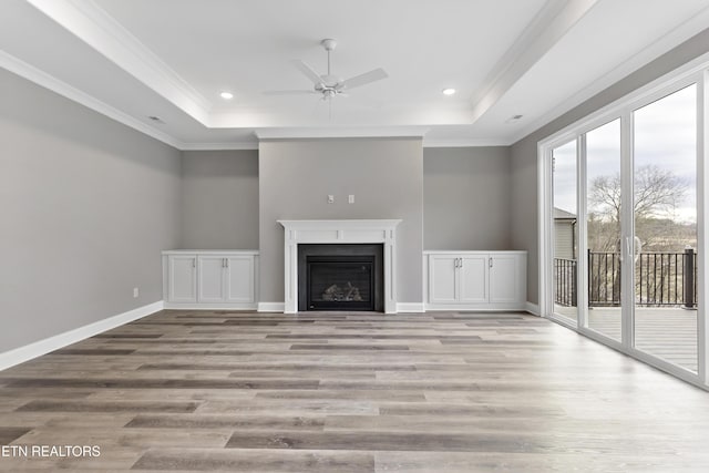 unfurnished living room featuring a raised ceiling, ornamental molding, ceiling fan, and light wood-type flooring