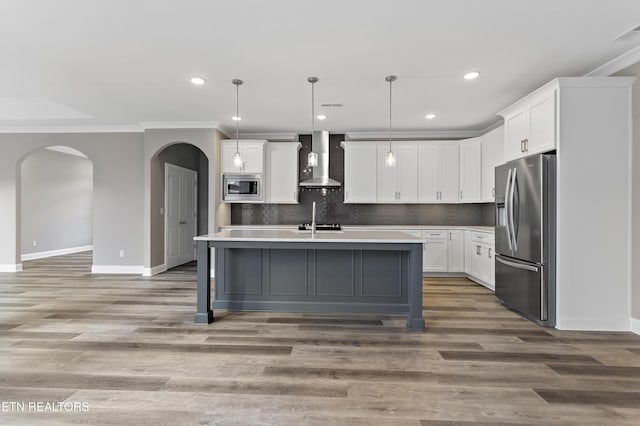 kitchen featuring appliances with stainless steel finishes, white cabinetry, hanging light fixtures, an island with sink, and wall chimney exhaust hood