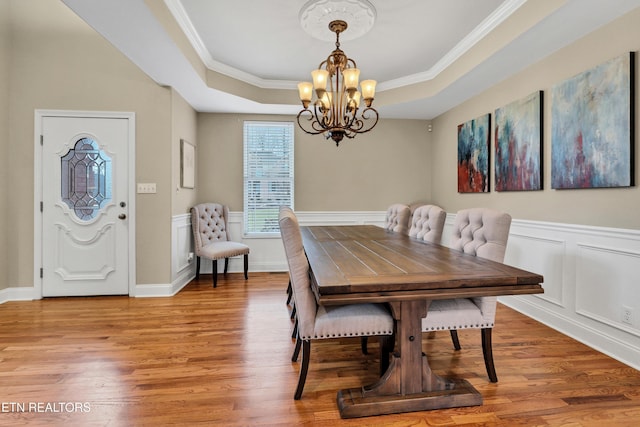 dining area with hardwood / wood-style flooring, ornamental molding, a raised ceiling, and a notable chandelier