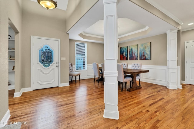 entryway featuring decorative columns, ornamental molding, a raised ceiling, and hardwood / wood-style floors