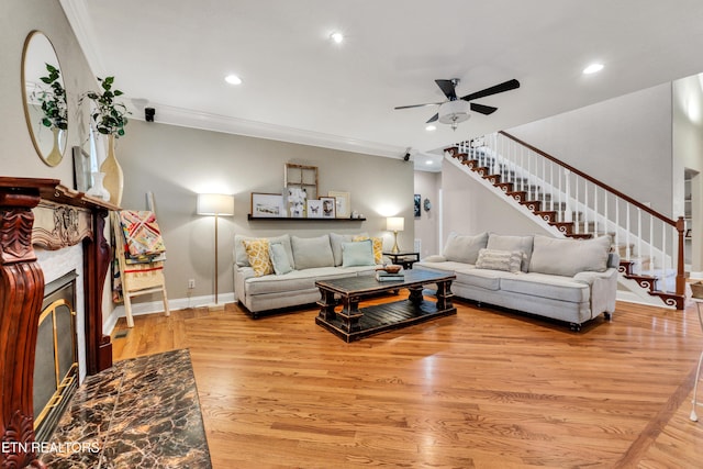 living room featuring a tile fireplace, ceiling fan, crown molding, and light hardwood / wood-style flooring