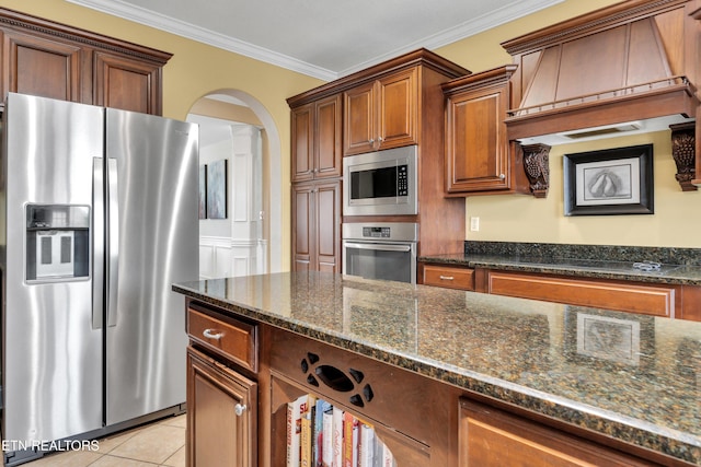 kitchen featuring appliances with stainless steel finishes, dark stone counters, ornamental molding, light tile patterned floors, and custom range hood