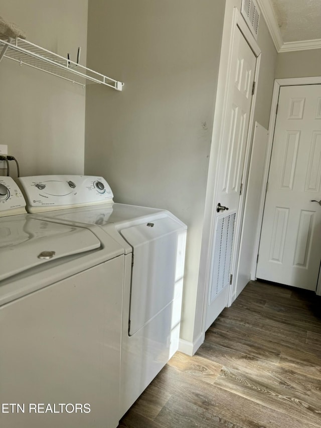 clothes washing area with washing machine and dryer, visible vents, crown molding, and wood finished floors