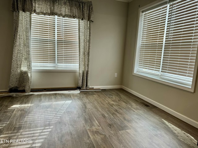 spare room featuring a healthy amount of sunlight, wood finished floors, visible vents, and baseboards