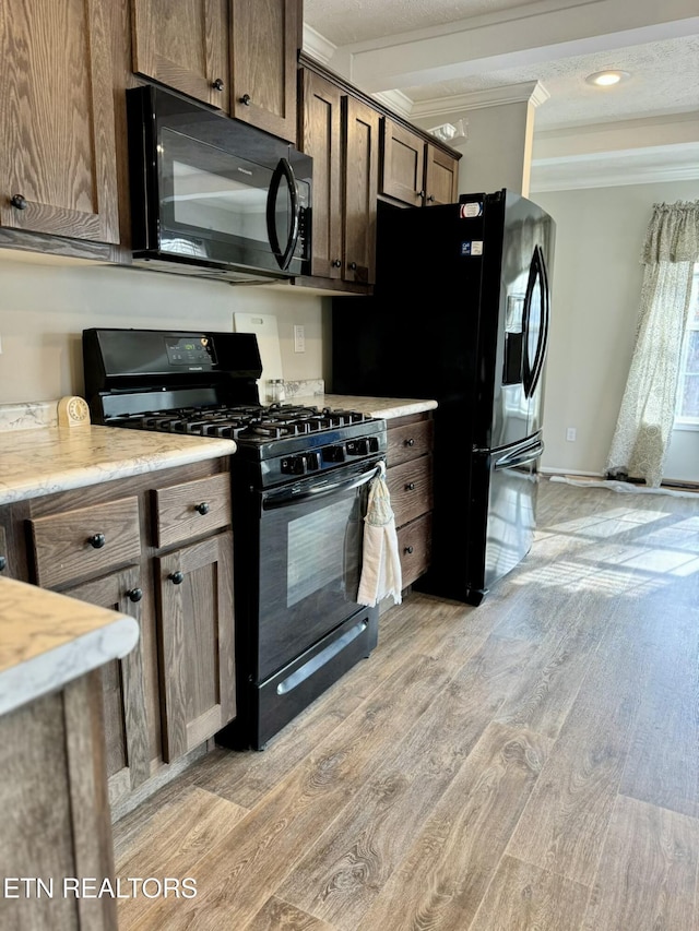 kitchen featuring crown molding, light wood finished floors, light countertops, dark brown cabinetry, and black appliances