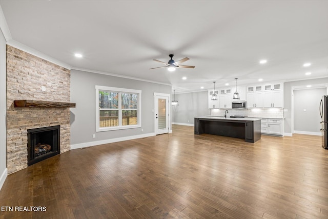 unfurnished living room featuring sink, crown molding, ceiling fan, a fireplace, and wood-type flooring