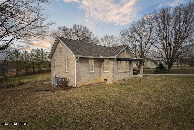 view of side of property with brick siding, a shingled roof, a lawn, fence, and cooling unit