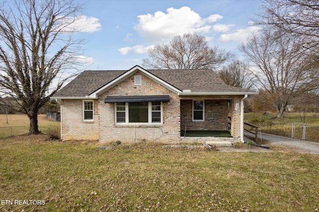 view of front of property with a shingled roof, fence, a front lawn, and brick siding