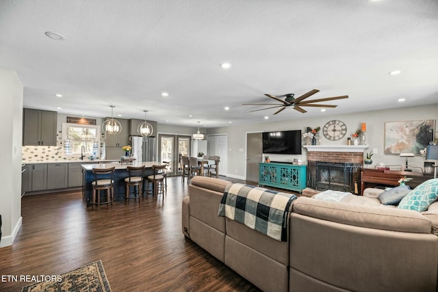 living room featuring a brick fireplace, sink, dark hardwood / wood-style floors, and ceiling fan