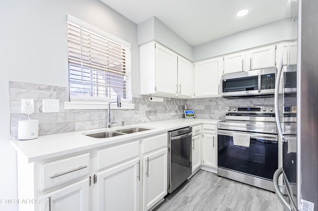 kitchen featuring appliances with stainless steel finishes, white cabinetry, sink, decorative backsplash, and light hardwood / wood-style floors