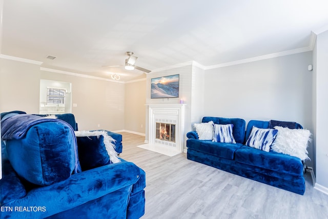 living room featuring a tile fireplace, ornamental molding, ceiling fan, and light wood-type flooring