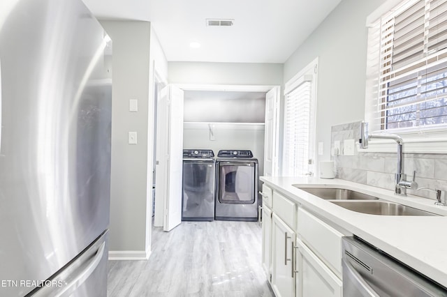 kitchen featuring sink, white cabinetry, washer and dryer, light wood-type flooring, and appliances with stainless steel finishes