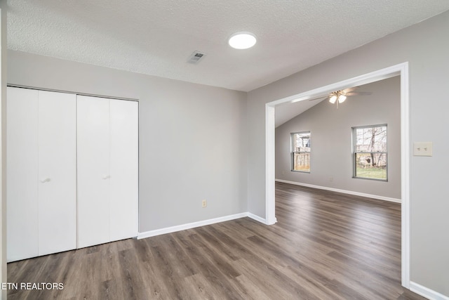 unfurnished bedroom featuring vaulted ceiling, a closet, hardwood / wood-style floors, and a textured ceiling