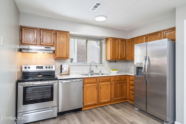 kitchen with sink, decorative backsplash, light stone counters, stainless steel appliances, and light hardwood / wood-style flooring