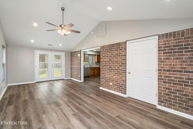 unfurnished living room featuring ceiling fan, brick wall, dark hardwood / wood-style flooring, vaulted ceiling, and french doors