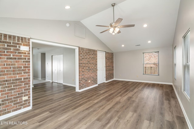 unfurnished living room featuring brick wall, dark hardwood / wood-style floors, high vaulted ceiling, and ceiling fan