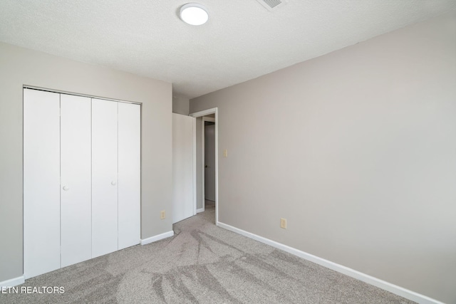 unfurnished bedroom with light colored carpet, a textured ceiling, and a closet