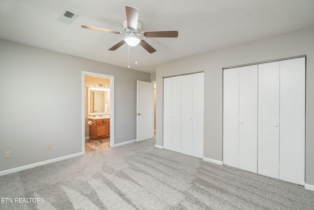 unfurnished bedroom with ensuite bath, light carpet, a textured ceiling, multiple closets, and ceiling fan