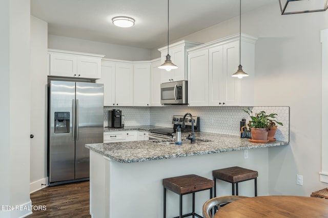 kitchen featuring pendant lighting, stainless steel appliances, kitchen peninsula, and white cabinets