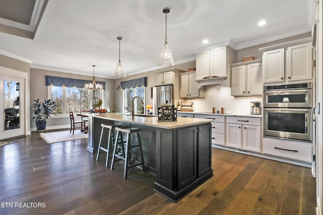 kitchen with a kitchen bar, sink, hanging light fixtures, a center island with sink, and stainless steel appliances