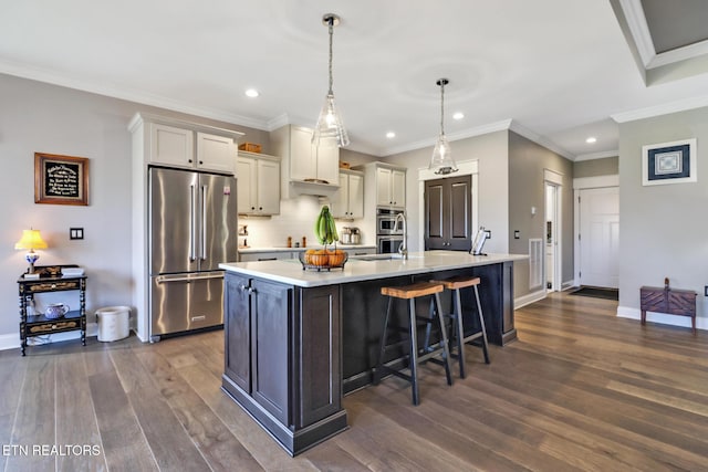 kitchen featuring a breakfast bar area, appliances with stainless steel finishes, hanging light fixtures, a center island with sink, and dark hardwood / wood-style flooring