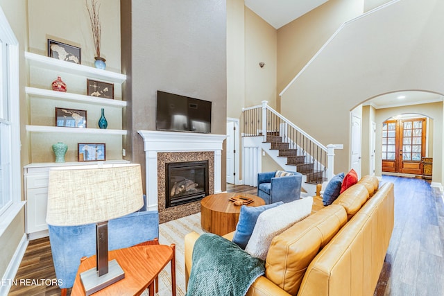 living room with dark wood-style floors, arched walkways, stairway, a high ceiling, and a premium fireplace