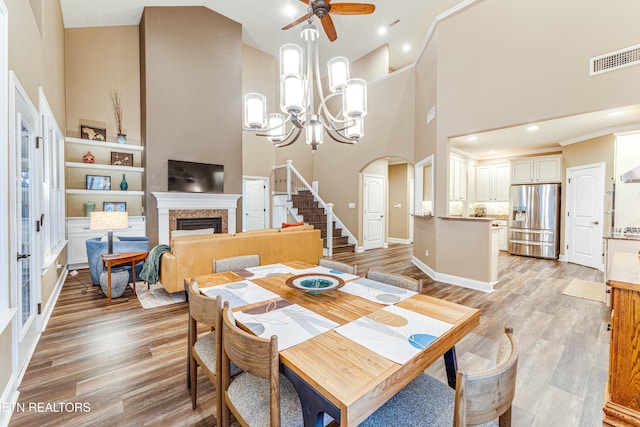 dining room with high vaulted ceiling, a fireplace, visible vents, stairway, and light wood-type flooring