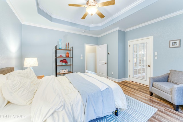 bedroom featuring a ceiling fan, baseboards, light wood-style floors, a tray ceiling, and crown molding