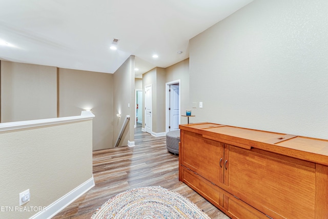 corridor featuring light wood finished floors, recessed lighting, baseboards, and an upstairs landing