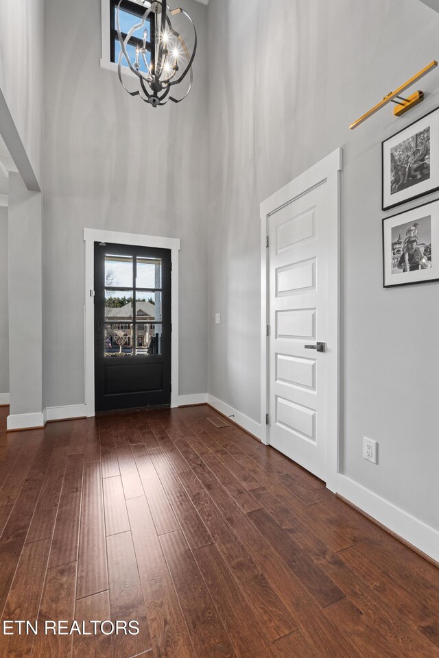 foyer with dark wood-type flooring, a towering ceiling, baseboards, and an inviting chandelier